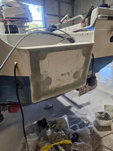 Boat's stern undergoing fiberglass repair in a workshop.