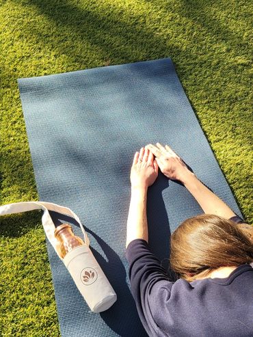 Person stretching on a yoga mat outdoors with a water bottle beside them.