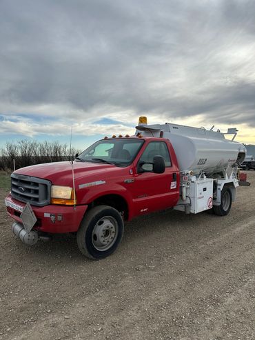 Red and white tanker truck on a gravel road under a cloudy sky.