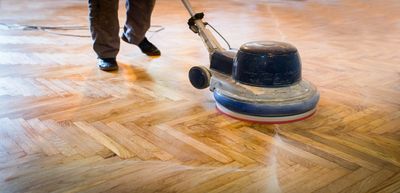 Person polishing a wooden floor with a floor buffer machine.