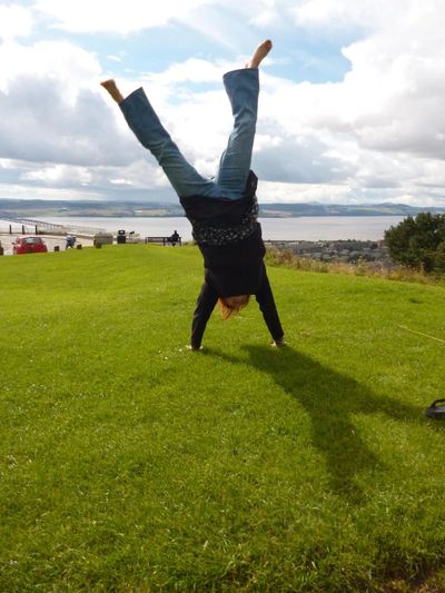 Emma is doing a handstand on grass, the Tay bridge and river are in background.