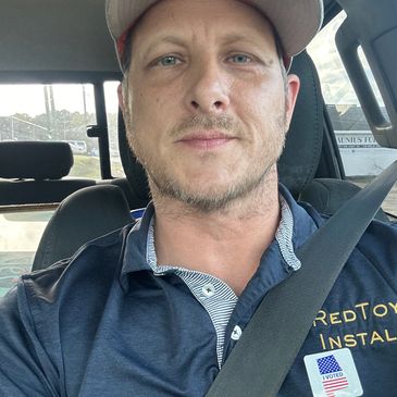Man wearing a cap and blue shirt in a car seat with a seatbelt.