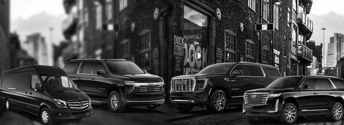 Four black luxury vehicles parked in front of a brick building in an urban setting.