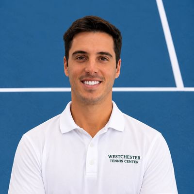 Smiling man in a white polo on a tennis court.