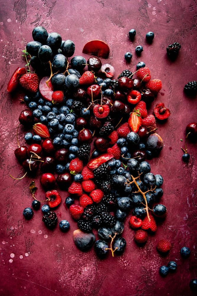 A vibrant assortment of berries and dark grapes on a textured purple surface.