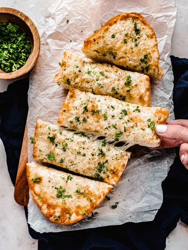 Slices of cheesy garlic bread garnished with fresh parsley on parchment paper.