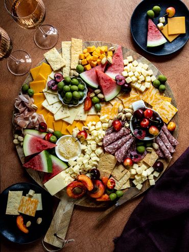A gourmet charcuterie board with cheeses, fruits, crackers, and wine glasses.