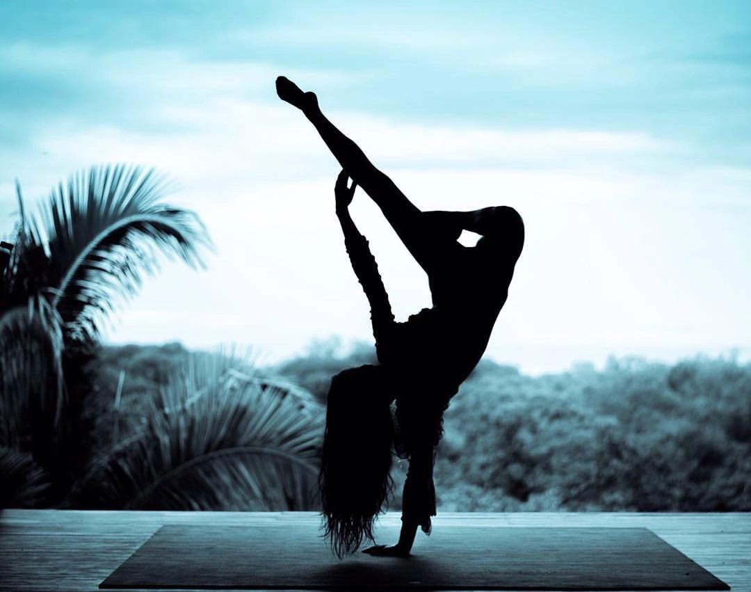 Silhouette of a person performing a high leg stretch yoga pose outdoors.