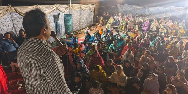 A man speaking to a large, attentive audience seated under a tent at night.