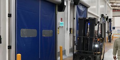 Montacargas operando en un almacén con puertas enrollables azules.