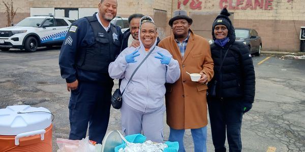 Group of five people smiling outdoors, with one making a peace sign and a police officer present.