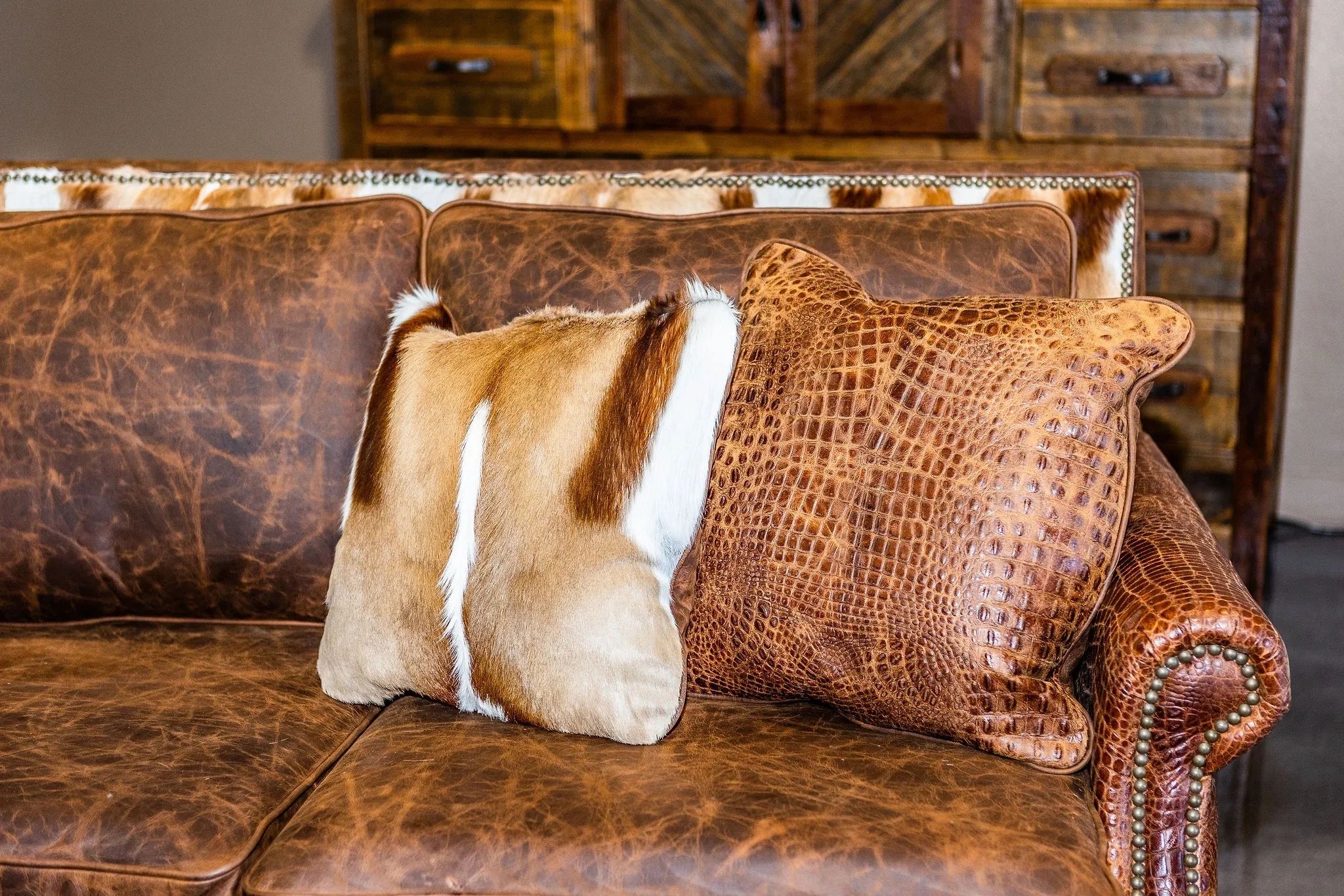 Two decorative leather and fur pillows on a brown leather couch.