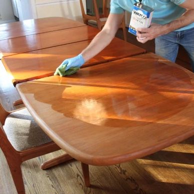 Person applying wood finish to a dining table with a cloth.