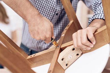 Person assembling wooden furniture using a screwdriver.