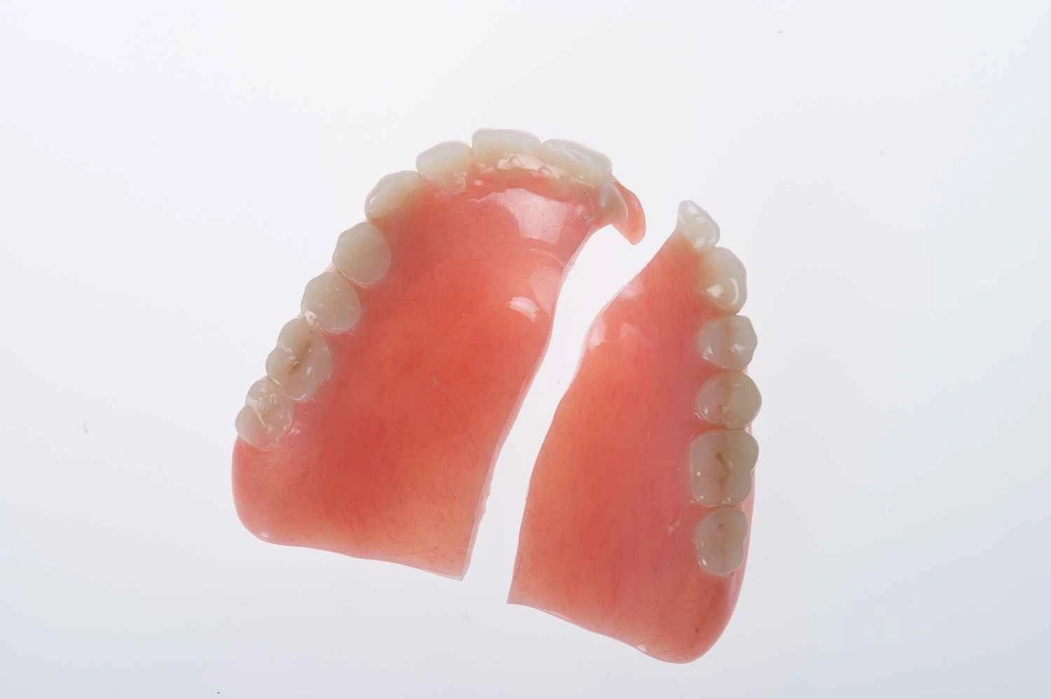 Broken upper denture with pink gum base and white teeth.