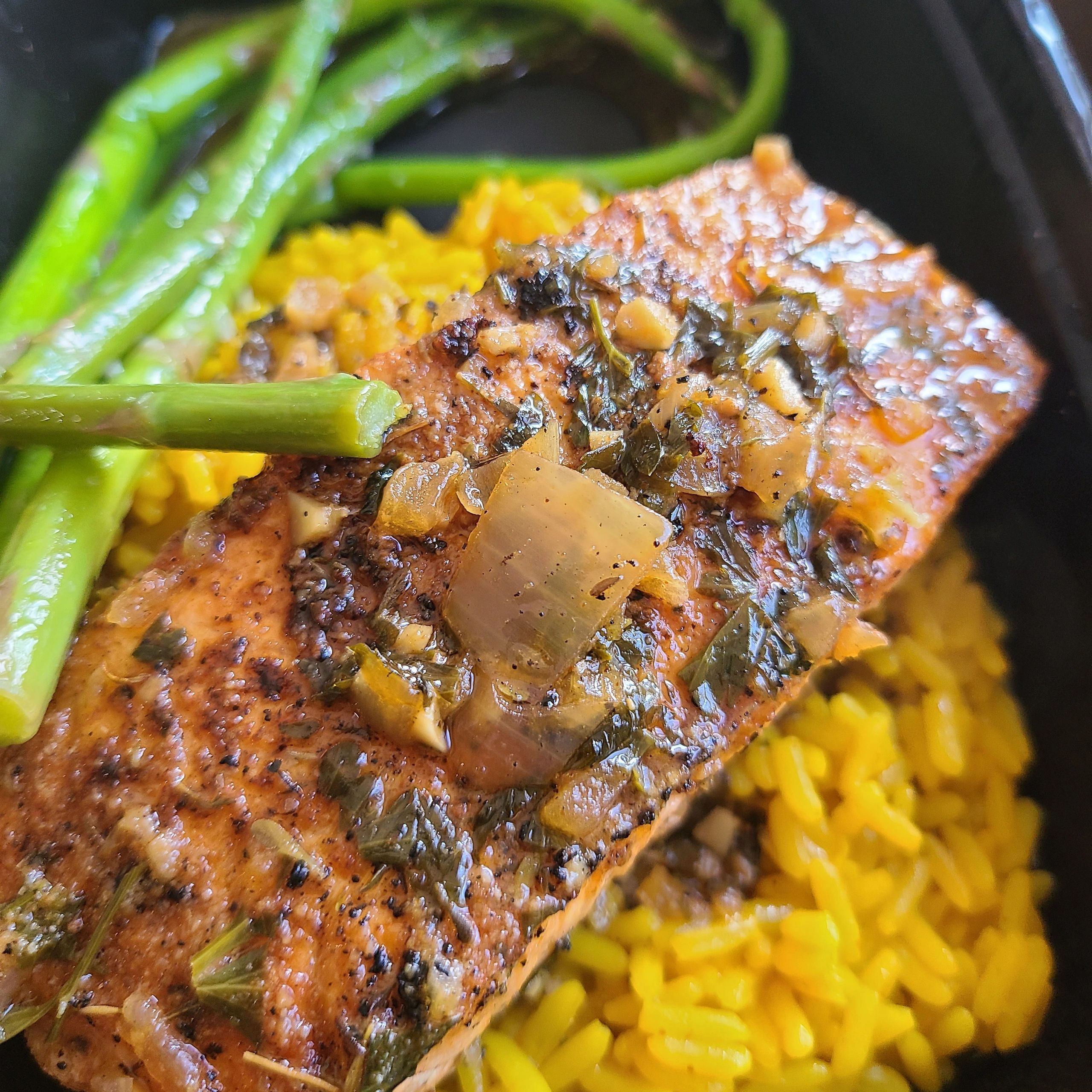salmon and yellow rice with asparagus in a black takeout container