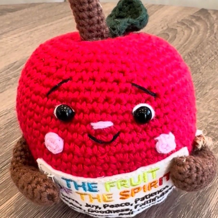 Crocheted red apple with a smiling face and a label.