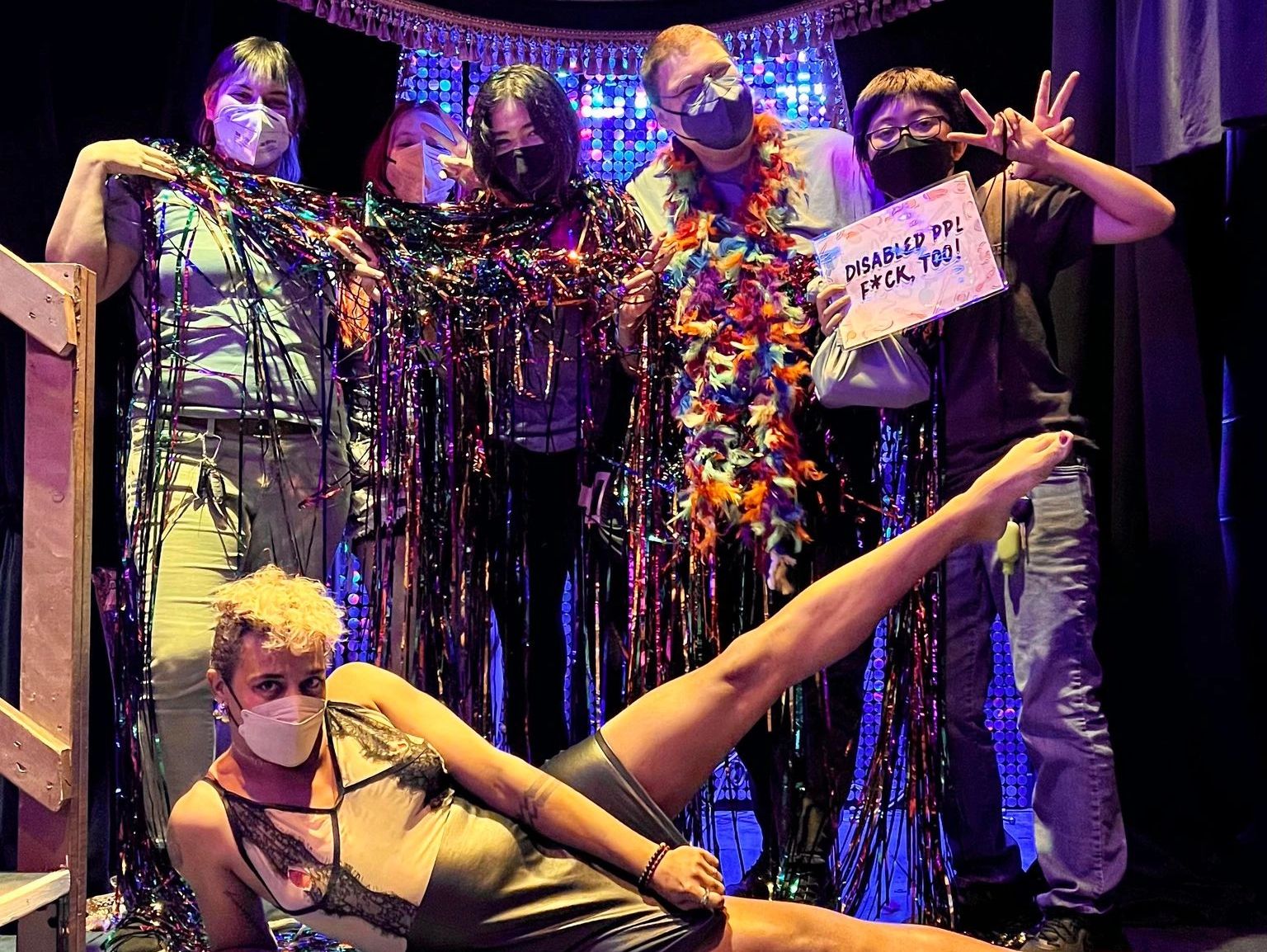 Group of people wearing face masks posing with props in front of a colorful backdrop.