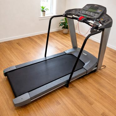 A modern treadmill in a bright room with wooden flooring and potted plants.