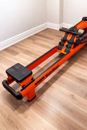Bright orange WaterRower rowing machine on wooden floor in a minimalist room.