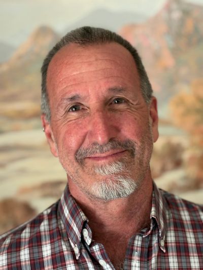 Smiling middle-aged man with a gray beard in a plaid shirt.