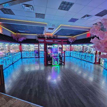 Brightly lit arcade claw machine room with neon blue lights and cherry blossom decor.