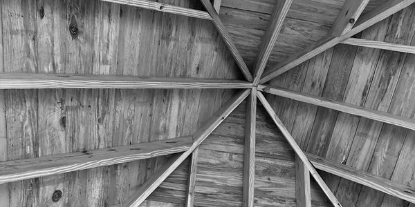 Black and white photo of a wooden roof structure with beams converging at the center.