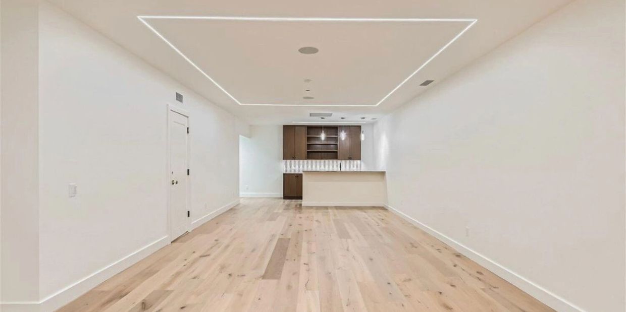 Modern empty room with light wood flooring and built-in bar area.