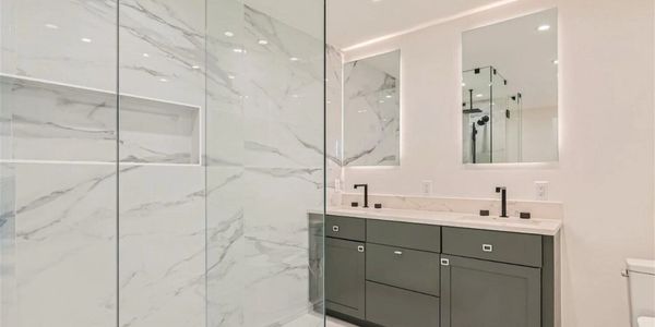 Modern bathroom with marble walls, glass shower, and double vanity sinks.
