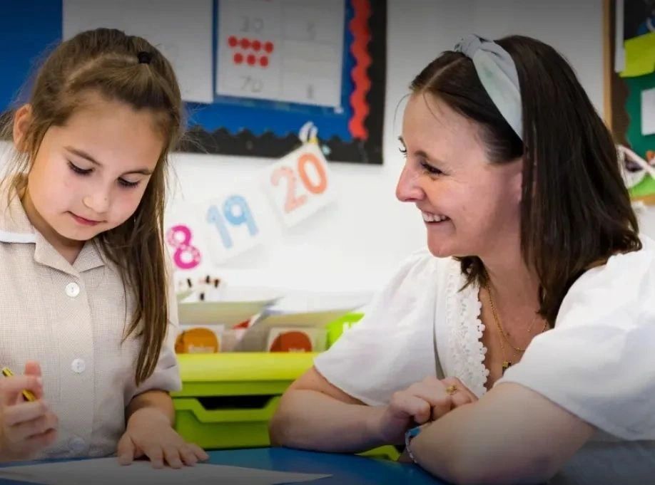 A teacher encourages a young student working on a task in a classroom.