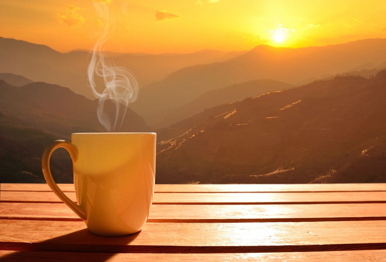 Steaming cup of coffee on a wooden table at sunrise in the mountains.