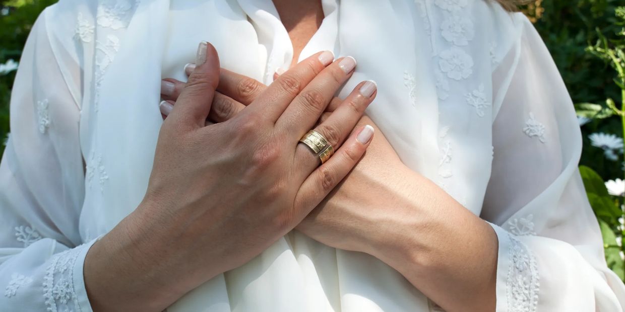 Hands crossed over chest wearing a gold ring on white floral fabric.