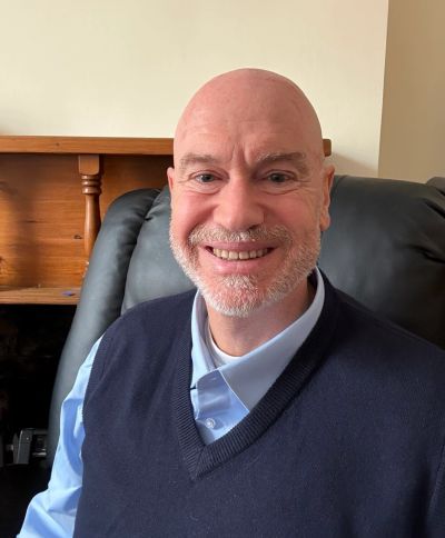 Smiling bald man with a beard sitting on a black chair.