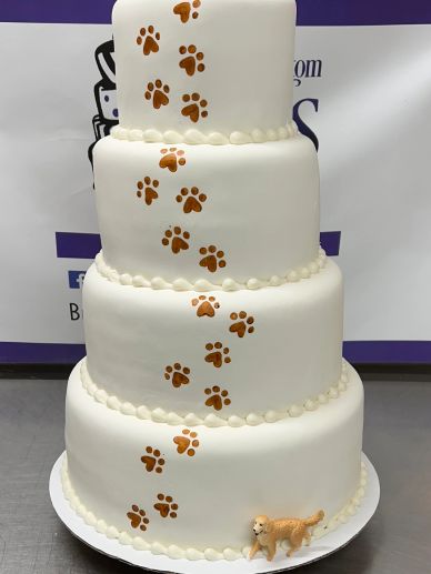 Four-tier white cake with brown paw prints and a small dog figurine.