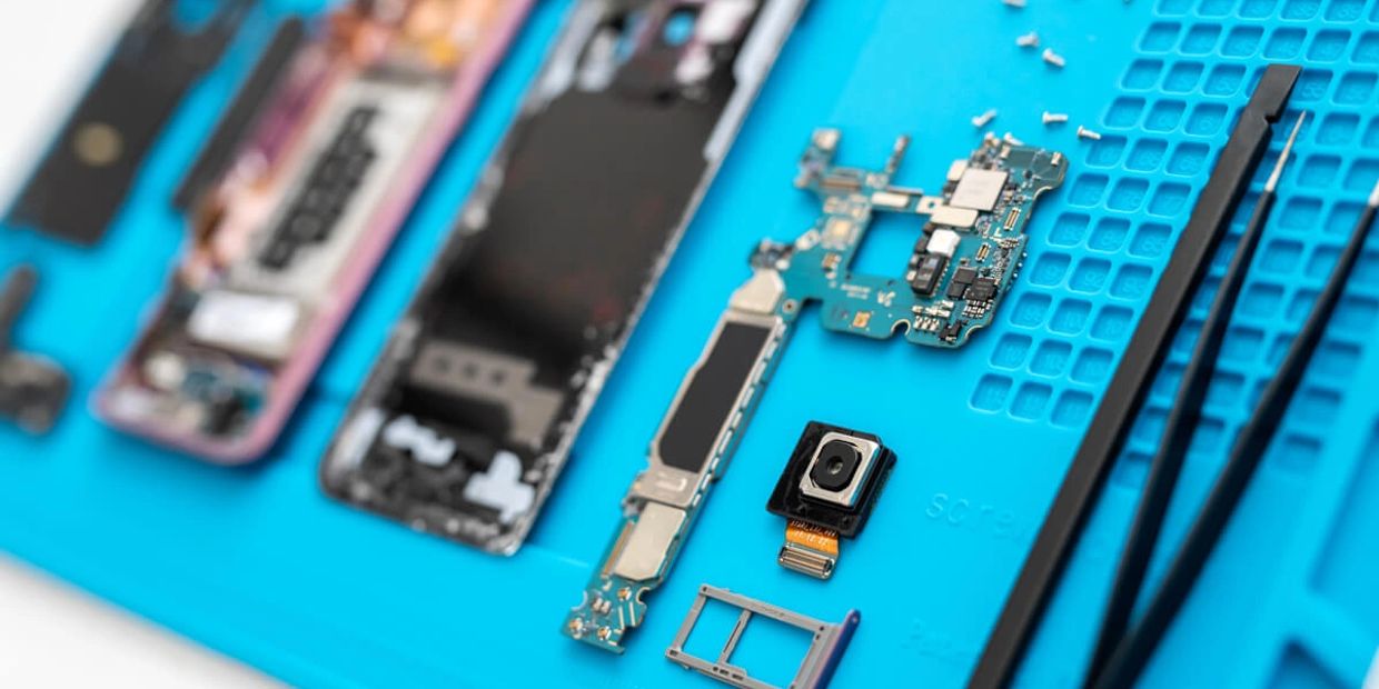 Componenti di uno smartphone smontato su un tappetino blu.