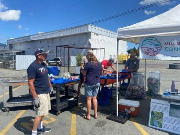 People sorting cans and bottles at an outdoor recycling event on a sunny day.