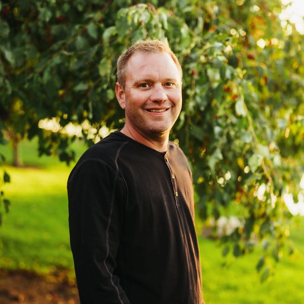 Smiling man outdoors with greenery in the background.
