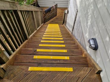 Wooden outdoor stairs with yellow anti-slip strips leading down to a small deck area.