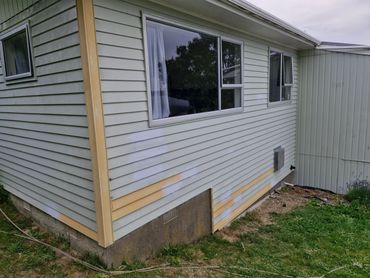 Exterior of a house with siding repairs and patch paint work near the foundation.