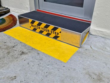 Metal step with a 'Watch Your Step' warning in front of a door.