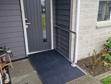 Accessible front entrance with a ramp and handrail beside a modern gray door.