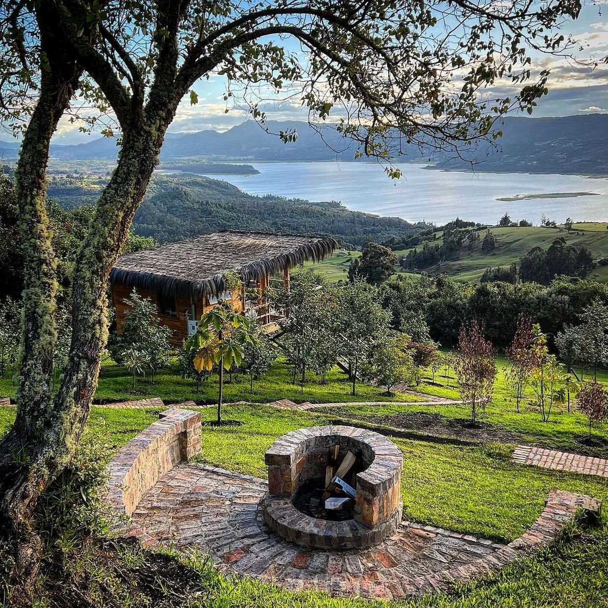 Scenic countryside with a thatched cabin, fire pit, and lake view.