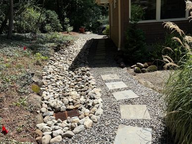 Stone walkway and drainage beside a house in a wooded area.