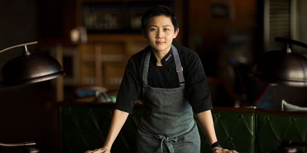 Chef in a striped apron standing confidently behind a wooden table.
