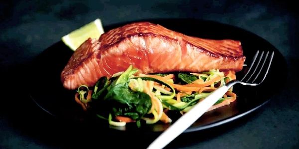 Grilled salmon fillet served on a bed of fresh sautéed vegetables with a lemon wedge.