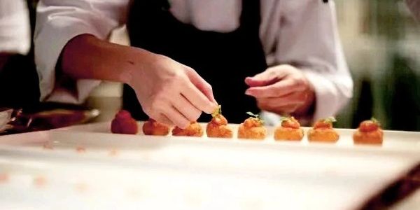 Chef delicately garnishing bite-sized appetizers on a tray.