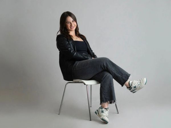 A woman in casual attire sitting on a chair, smiling warmly.