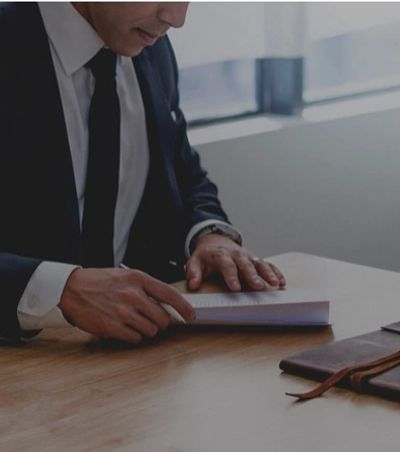 Businessman in suit reading a book at a desk.