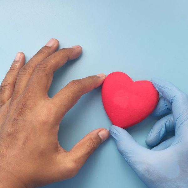 Two hands reaching for a red heart on a blue surface.