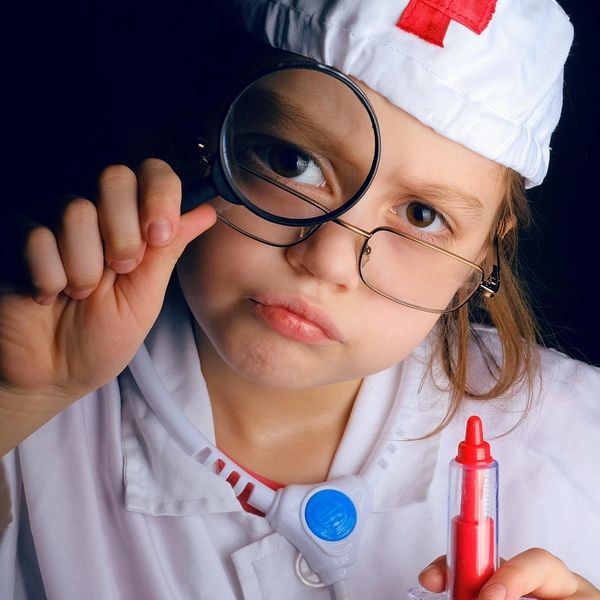 Child dressed as a doctor examining with a magnifying glass and holding a toy syringe.